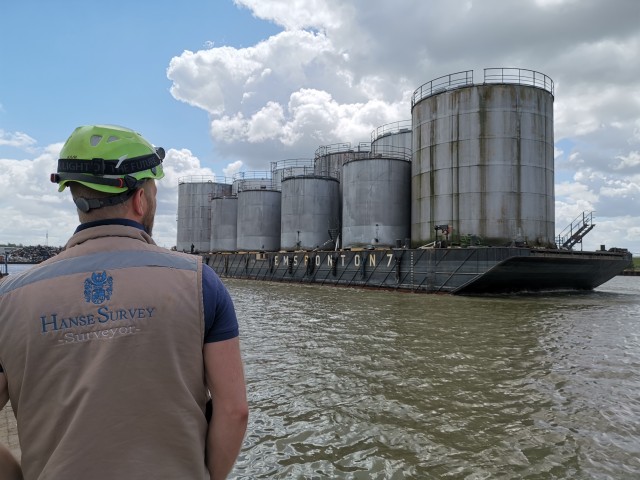 Surveyor observes transport of silo tanks by pontoon