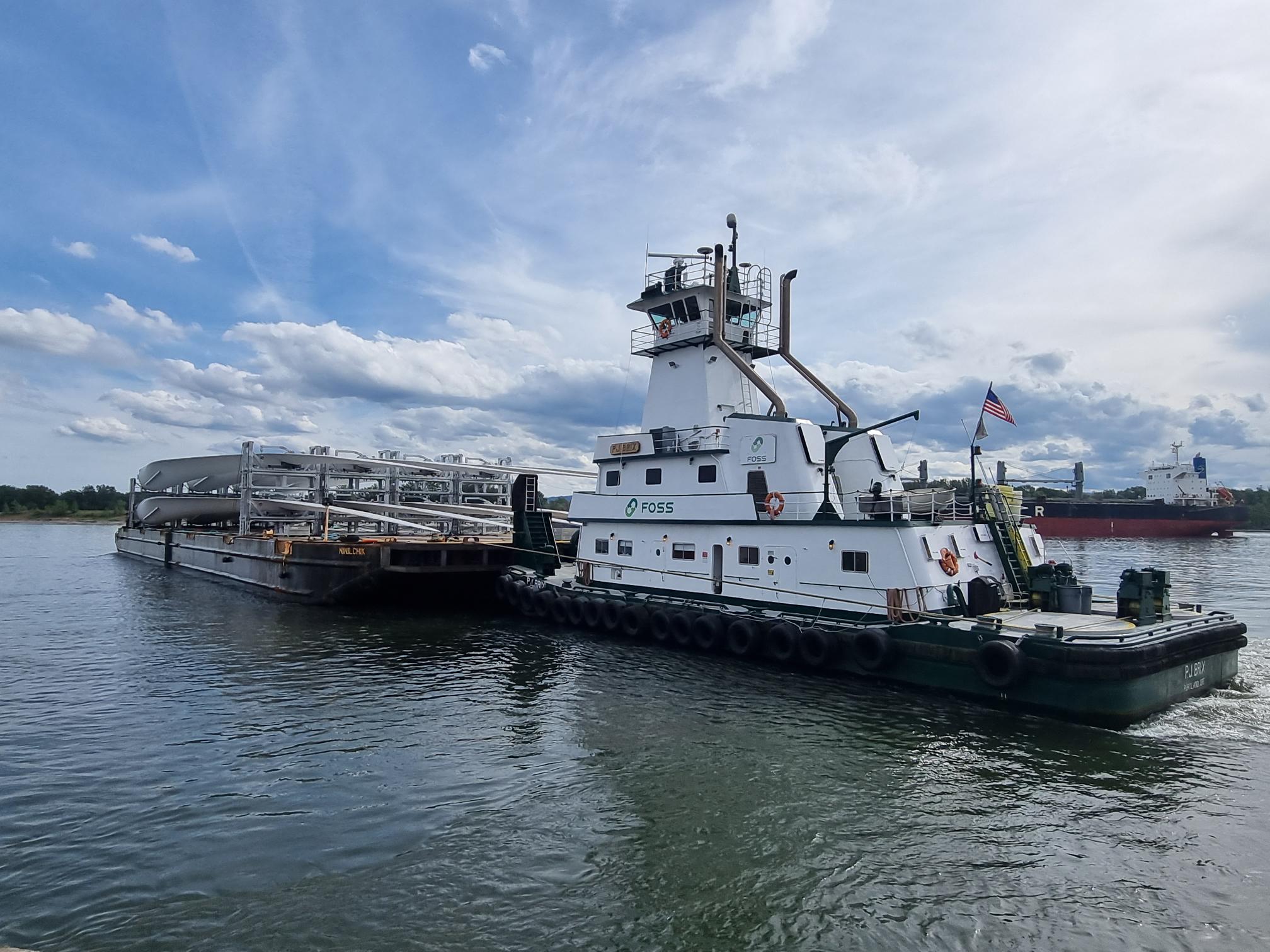 Pontoon with blades of a wind turbine is pushed by a tugboat