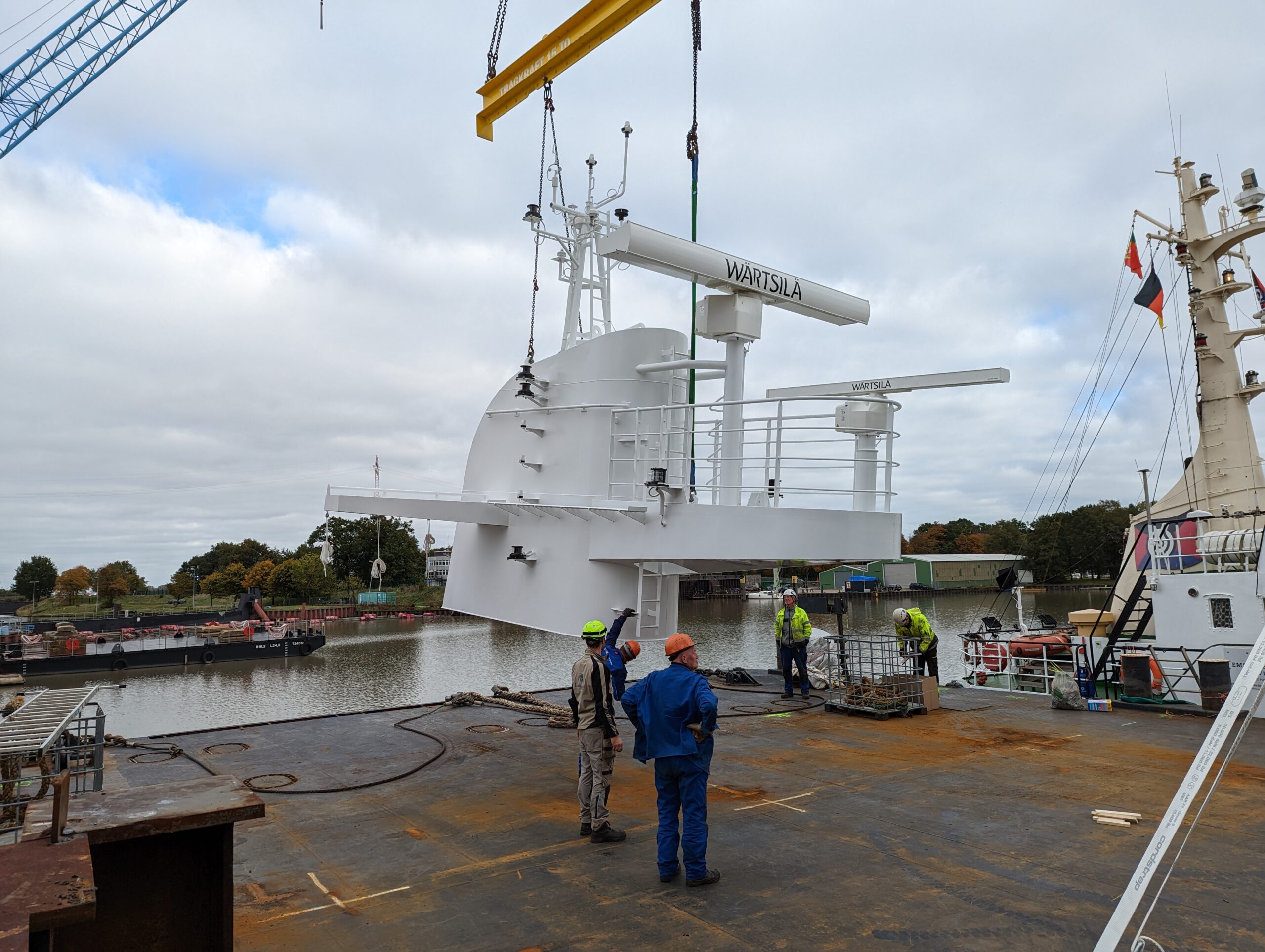Heavy cargo is lifted onto the deck of a pontoon with the help of a spreader beam and a crane